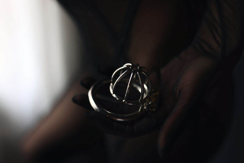 A chastity ring set resting in a gloved palm, shot close and shallow.