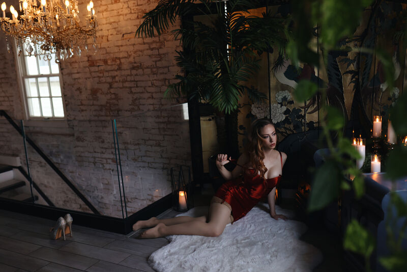 A candlelit room with a chandelier, Goddess Nikki Kit small in the frame in a red dress.